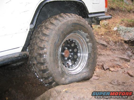 Flat tire on a white off-road vehicle with chrome wheels, stuck on muddy terrain