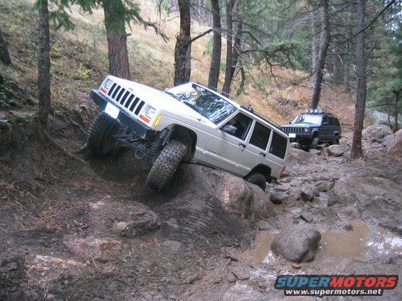 Silver 1997 Jeep Cherokee on a rocky, muddy trail, with a black Jeep Cherokee behind it