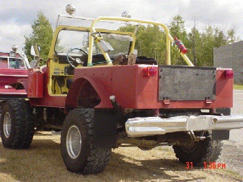 1976 Jeep CJ7, red body, yellow roll cage, large tires, parked next to a red truck
