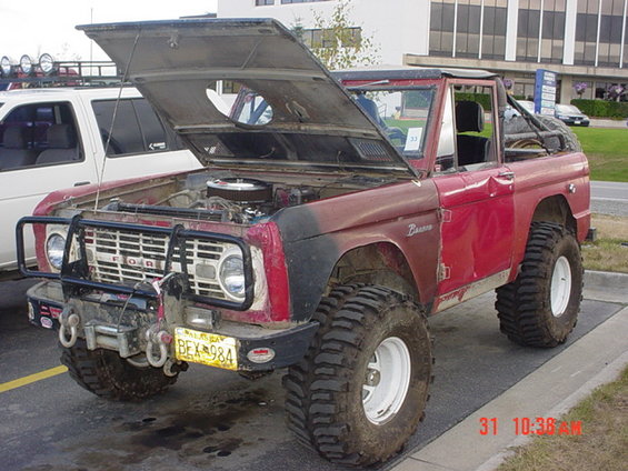 Red Ford Bronco with hood open, large off-road tires, and a winch