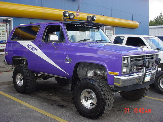 Purple lifted SUV with off-road tires, white stripe graphic reading "GOT MUD?", and KC lights on the roof