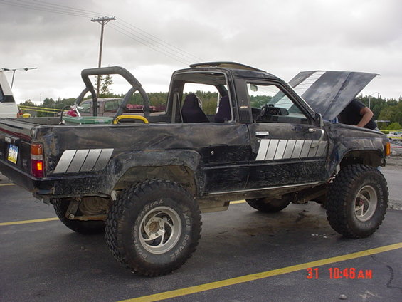 Black pickup truck with roll bar, lifted suspension, and off-road tires. Hood is open with a person underneath