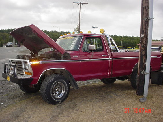 Red Ford F-Series pickup with hood open, off-road tires, and smiley face lights on roof