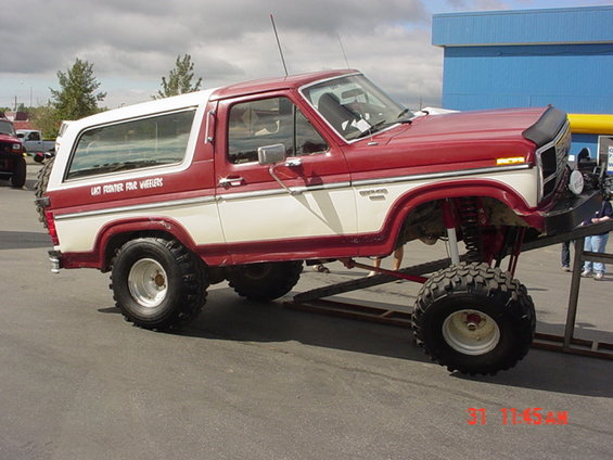 Lifted red and white Ford Bronco on display, side view, with custom wheels and tires