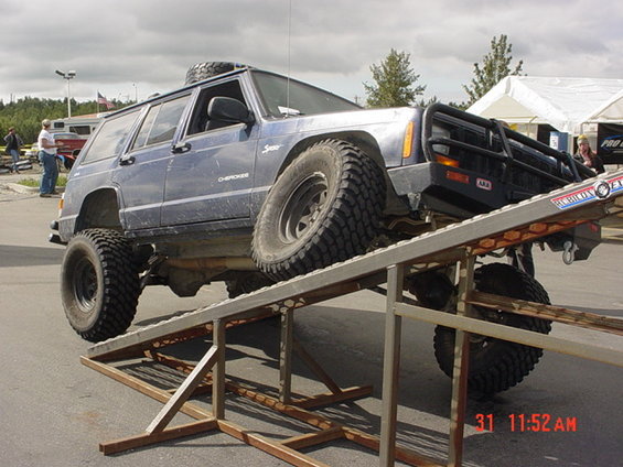 Blue Jeep Cherokee XJ on a metal ramp, spare tire on roof