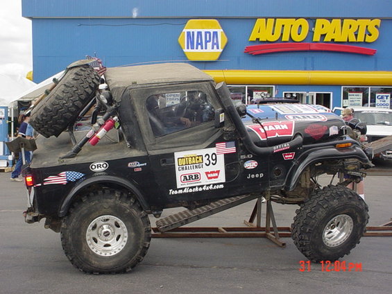 Modified Jeep CJ with spare tire on back, snorkel, and off-road tires parked in front of a NAPA Auto Parts store