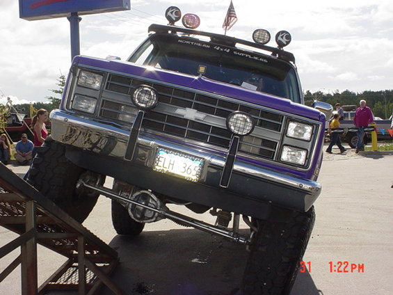 Purple Chevrolet pickup truck with lifted suspension on a ramp, showing front grille and license plate ELH 365