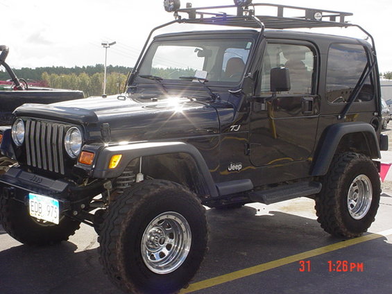Black Jeep Wrangler TJ with roof rack and off-road tires parked on asphalt