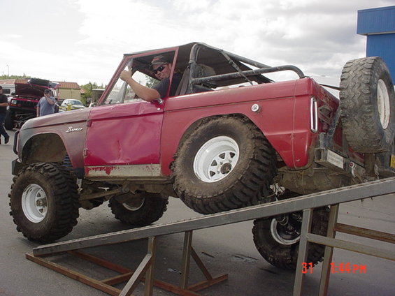 Red 1976 Ford Bronco on ramps, driver gives thumbs up. Visible text 'Bronco'