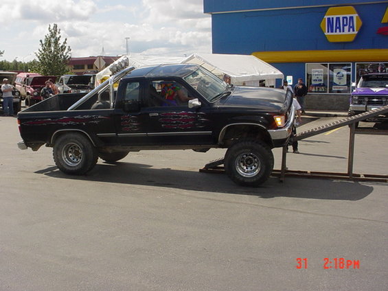 black pickup truck with custom flame decals, lifted, on ramps in front of a NAPA store
