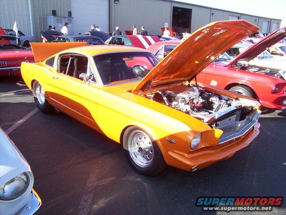 Orange 1965 Ford Mustang fastback, hood open, showing engine. Chrome wheels