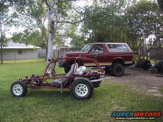 Maroon and tan Ford Bronco, 3/4 front view, parked on grass next to a dune buggy