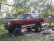 1990 Ford Bronco - This lifted Ford Bronco is parked in a yard with trees and a fence in the background.