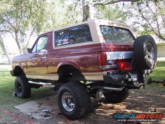 Maroon and tan Ford Bronco with a spare tire mounted on the rear, lifted on large tires