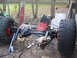 1990 Ford Bronco - Vehicle axles and large tires are shown disassembled outdoors, with various scrap materials in the background.