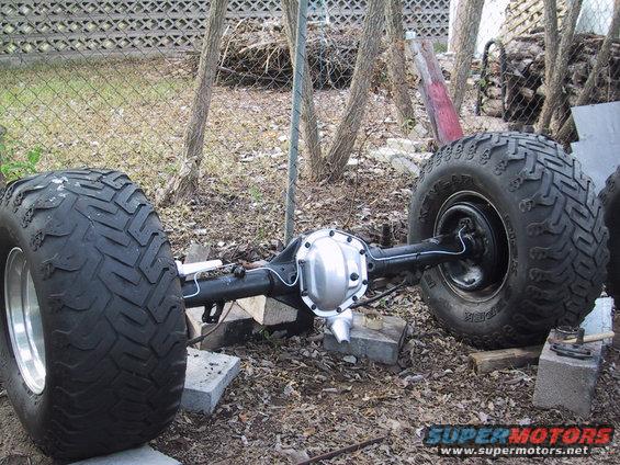 Rear axle assembly with two large, knobby tires, resting on cinder blocks outdoors