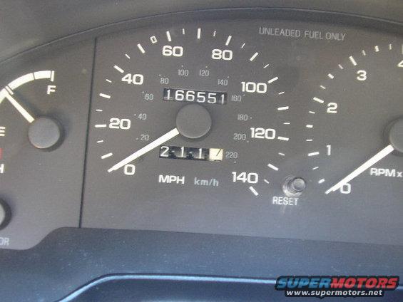 Car dashboard with speedometer, fuel gauge, and odometer showing 166551 miles