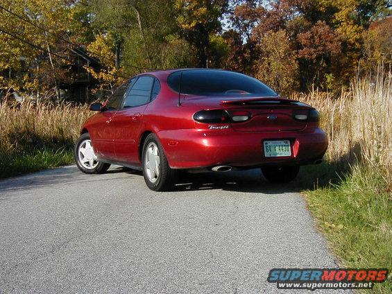 Red sedan parked on a road with trees and tall grass in the background