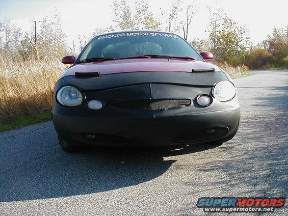 Front view of a red 1997 Ford Taurus with a black car bra and "ANONDA MOTORSPORTS" banner