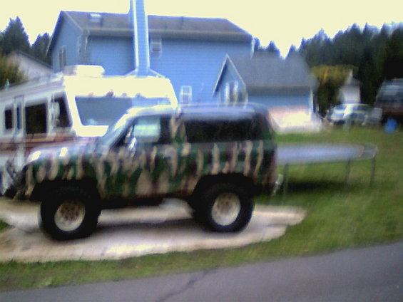 Camouflage SUV parked on concrete pad, side view. White wheels, dark tinted windows
