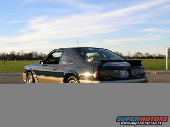 1989 Ford Mustang coupe, rear 3/4 view, dark color with tan lower body, aftermarket spoiler, license plate ME 2970