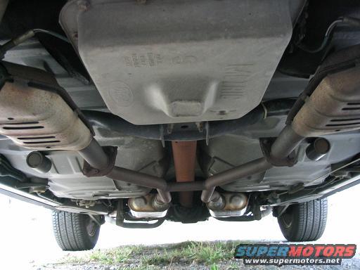 Undercarriage view of a vehicle's exhaust system and drivetrain components, with visible Supermotors.net watermark