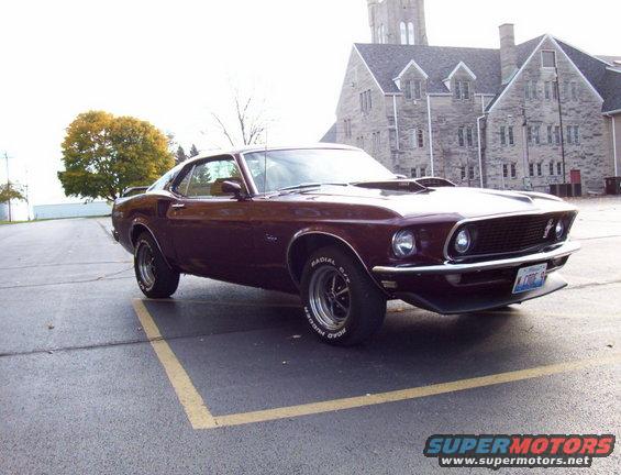 1969 Ford Mustang parked in a lot with a stone building behind it