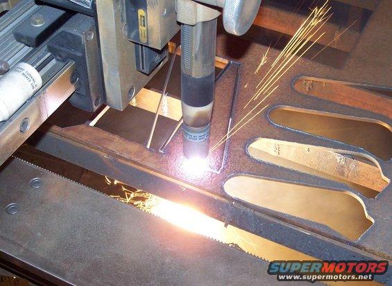 Plasma cutter torch creating sparks while cutting metal shapes, with Supermotors logo visible