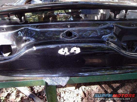 Black car trunk lid with dented area and white primer spots