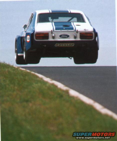 race car with blue stripes on white body, rear view, airborne over track