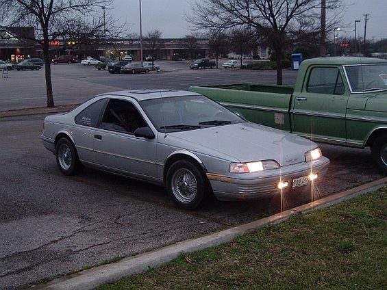 Silver 1992 Ford Thunderbird parked in a lot next to a green pickup truck