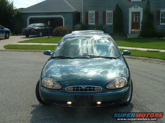 Front view of a dark green sedan with a sunroof parked in a driveway. Another car is in the garage behind it