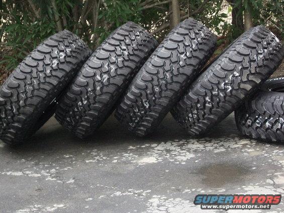 Four off-road tires with aggressive tread patterns leaning against each other on a concrete surface