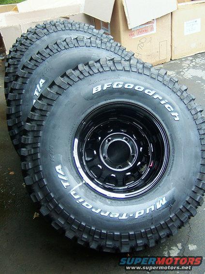 Three BFGoodrich Mud-Terrain T/A tires mounted on black steel rims, stacked in a row
