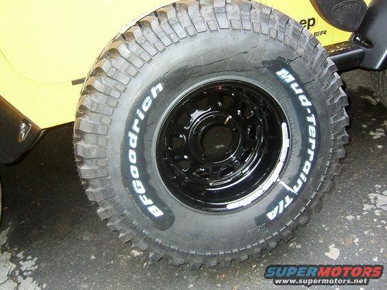 Close-up of a BFGoodrich Mud-Terrain T/A tire on a black rim, with part of a yellow vehicle visible