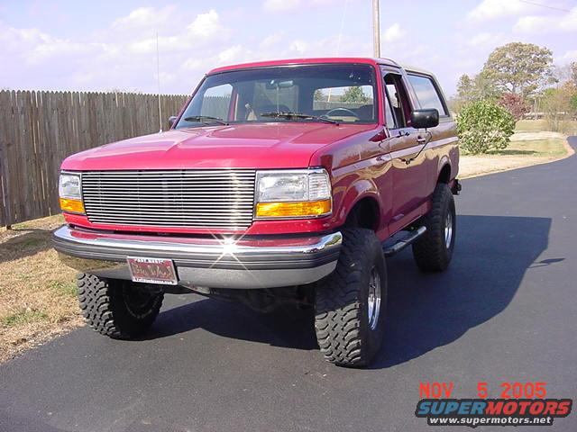 Red Ford Bronco with chrome grille and large off-road tires, viewed from a 3/4 front angle