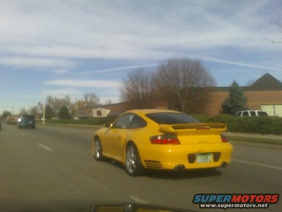 Yellow Porsche 911 with a large rear spoiler driving on a highway