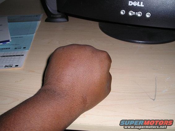 Fist on a wooden desk next to a Dell monitor and papers