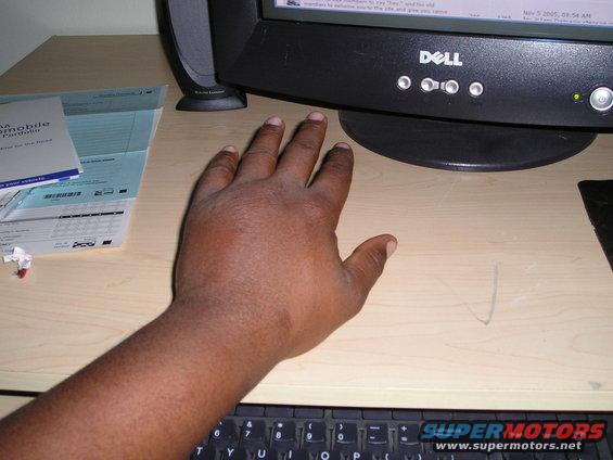 Hand resting on a wooden desk next to a Dell computer monitor and keyboard