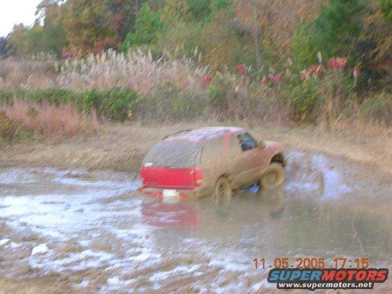 Red SUV driving through mud, rear view. Watermark reads 11.05.2005 17:15 SUPERMOTORS