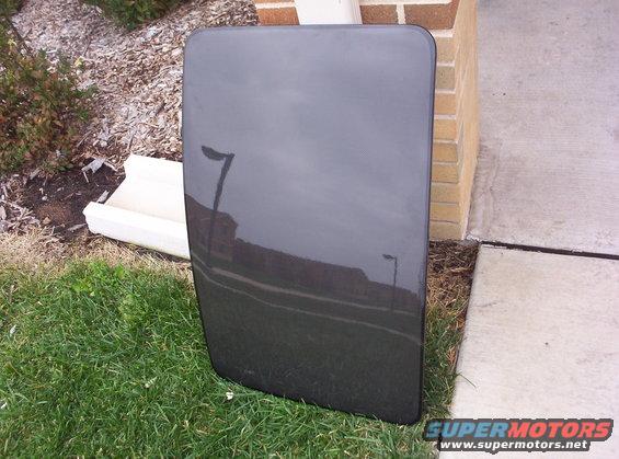 Dark gray car roof panel resting on grass next to a brick wall