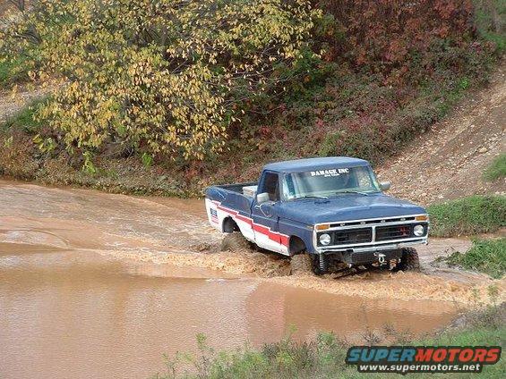 1977 Ford F-150 driving through water, blue with red stripe