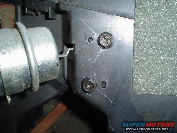 Close-up of a black plastic panel with two screws and a metal component on the left