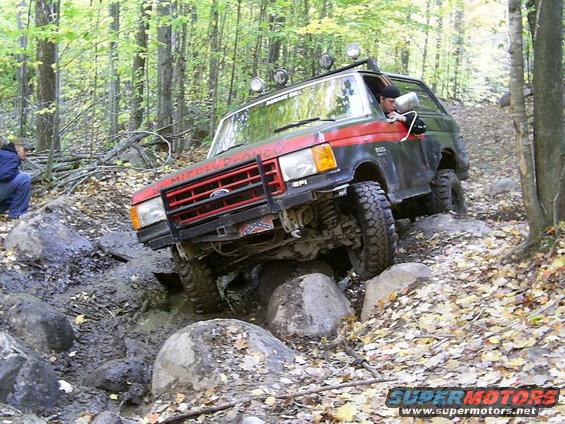 Red and black off-road SUV on rocky trail, front grille visible