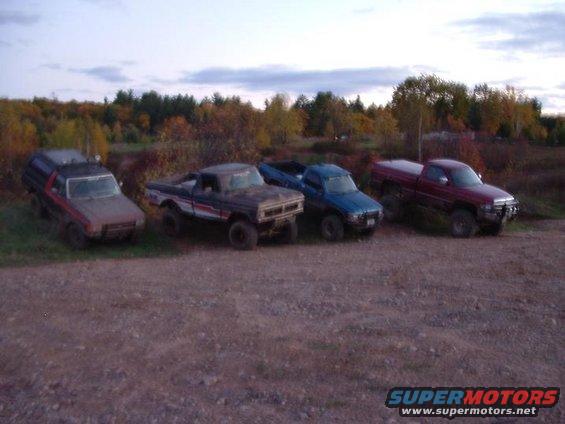 Four pickup trucks and a camper shell parked outdoors