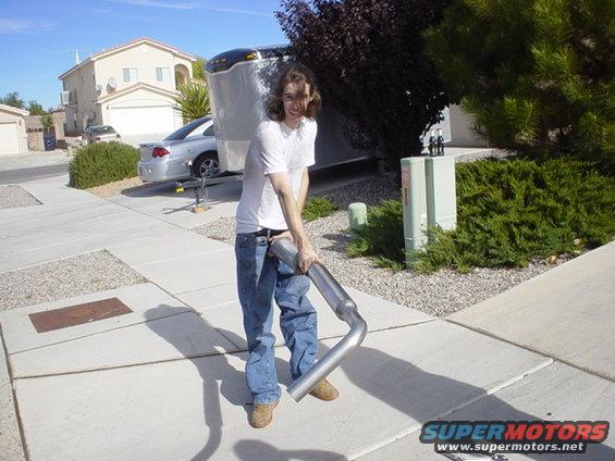 man holding exhaust pipe in front of trailer and silver car