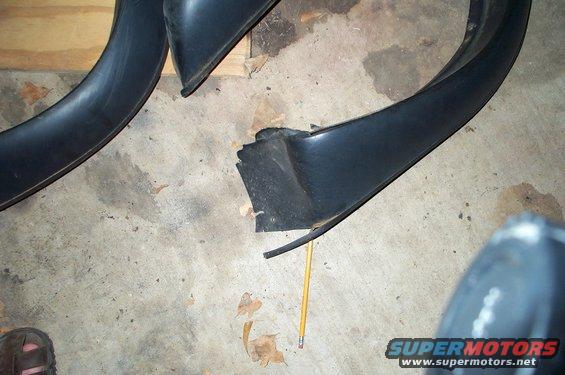 two black plastic fender flares, one is broken, lying on a concrete floor