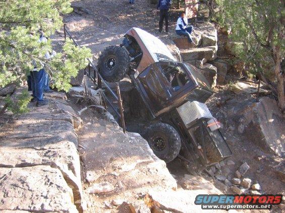 Off-road vehicle tilted precariously on rocky terrain, with people observing
