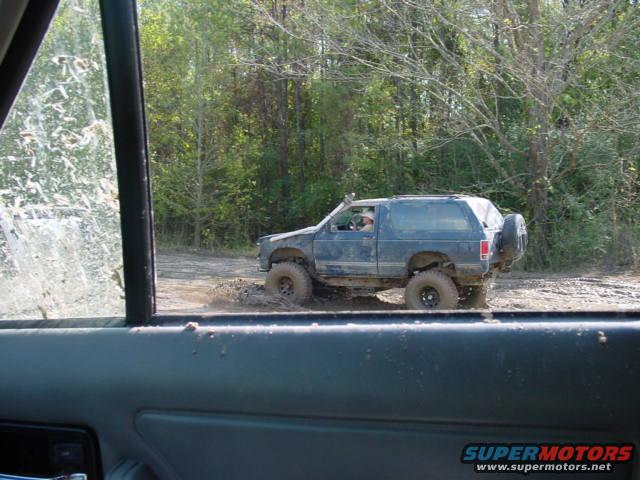 Dark blue SUV driving through mud, spare tire on rear door, aftermarket wheels
