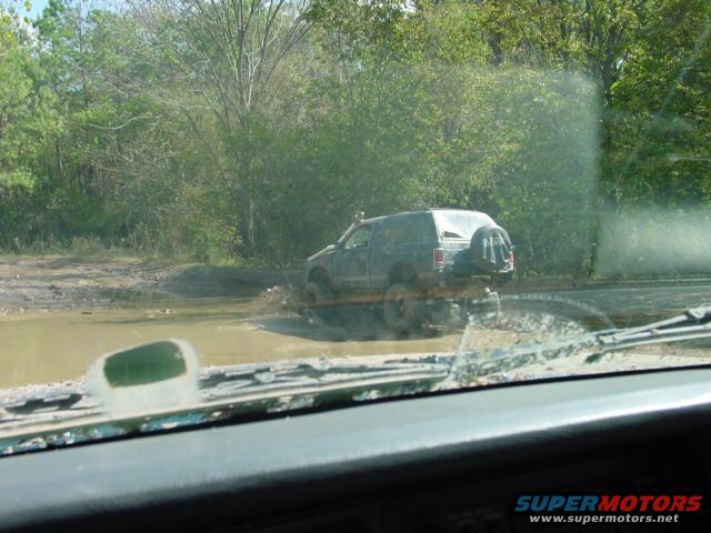 Dark SUV with spare tire on back driving through mud puddle